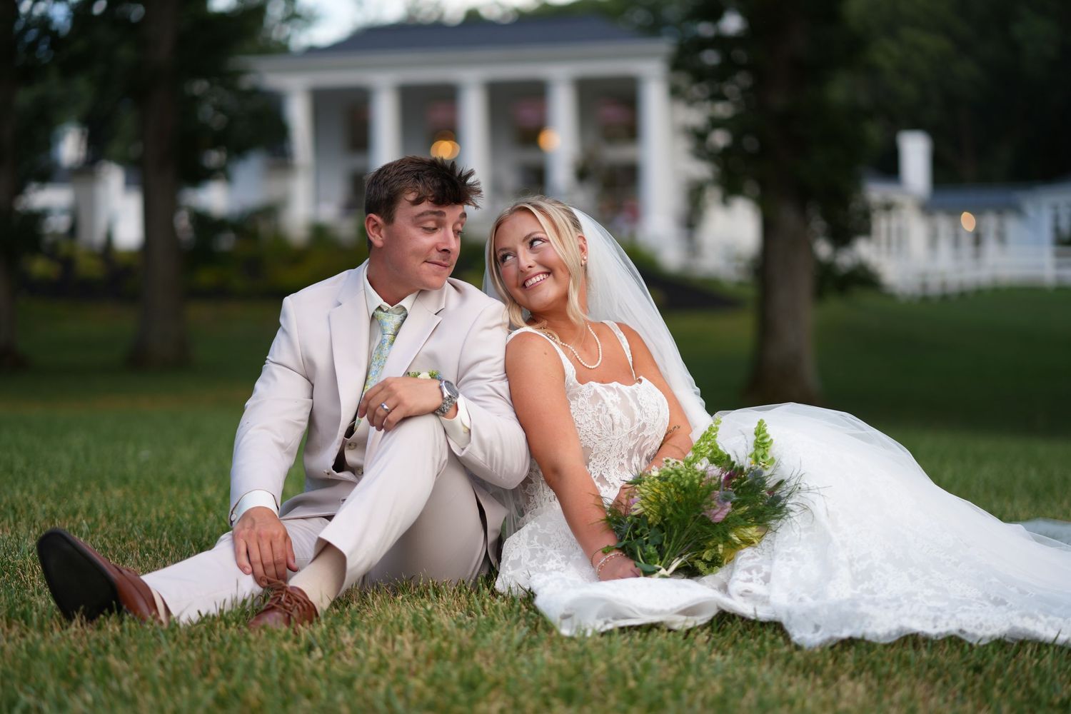 bride and groom resting in front of historic white estate home in Mebane, NC