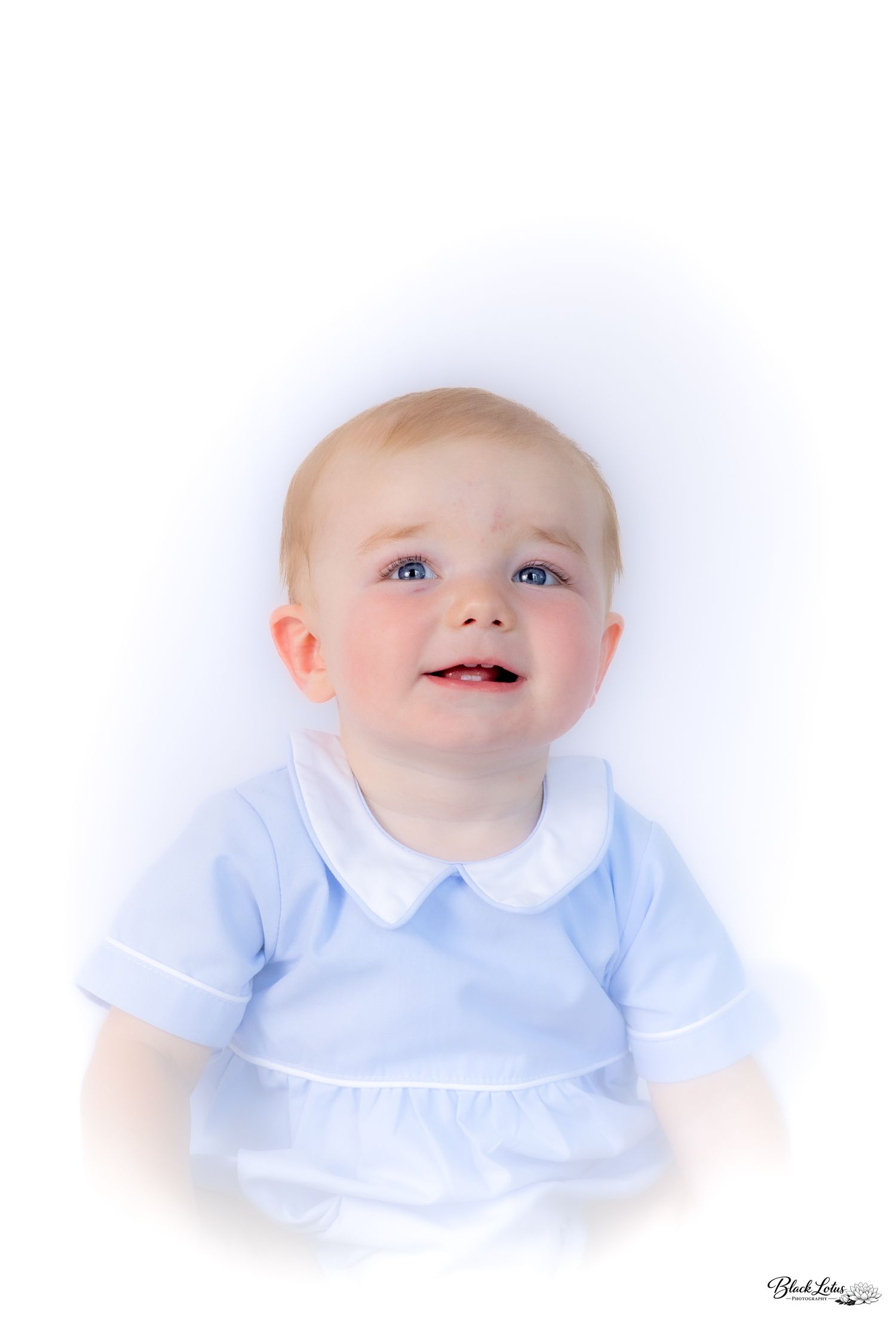 Adorable baby in light blue Peter Pan collar outfit smiling and looking up against white background.