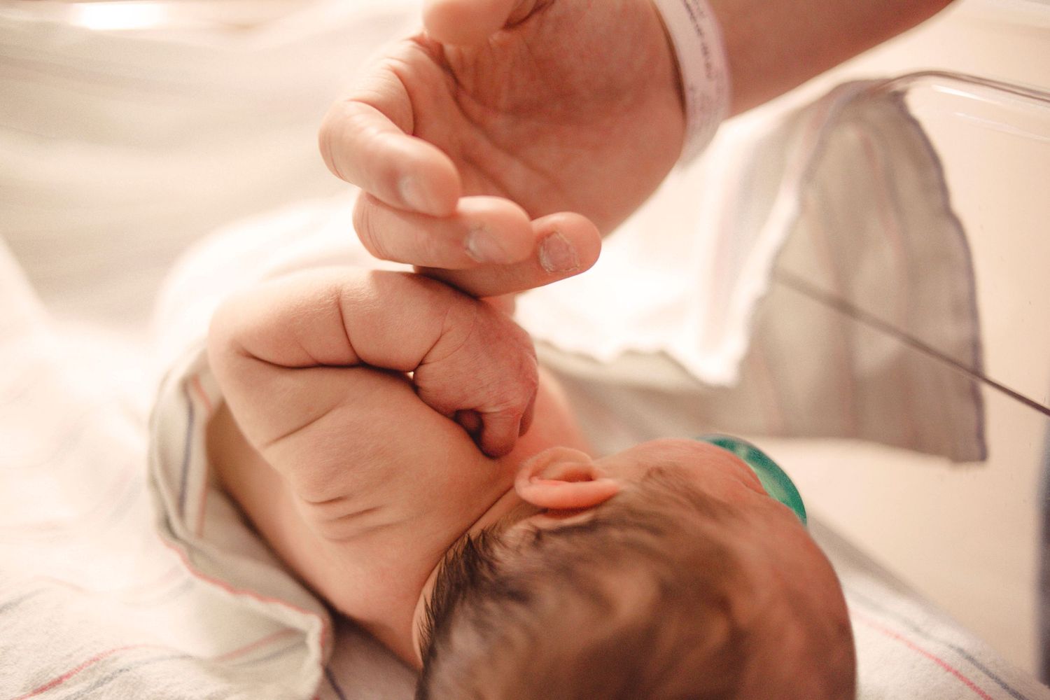 Newborn baby grasping an adult finger while lying in hospital blanket after birth.