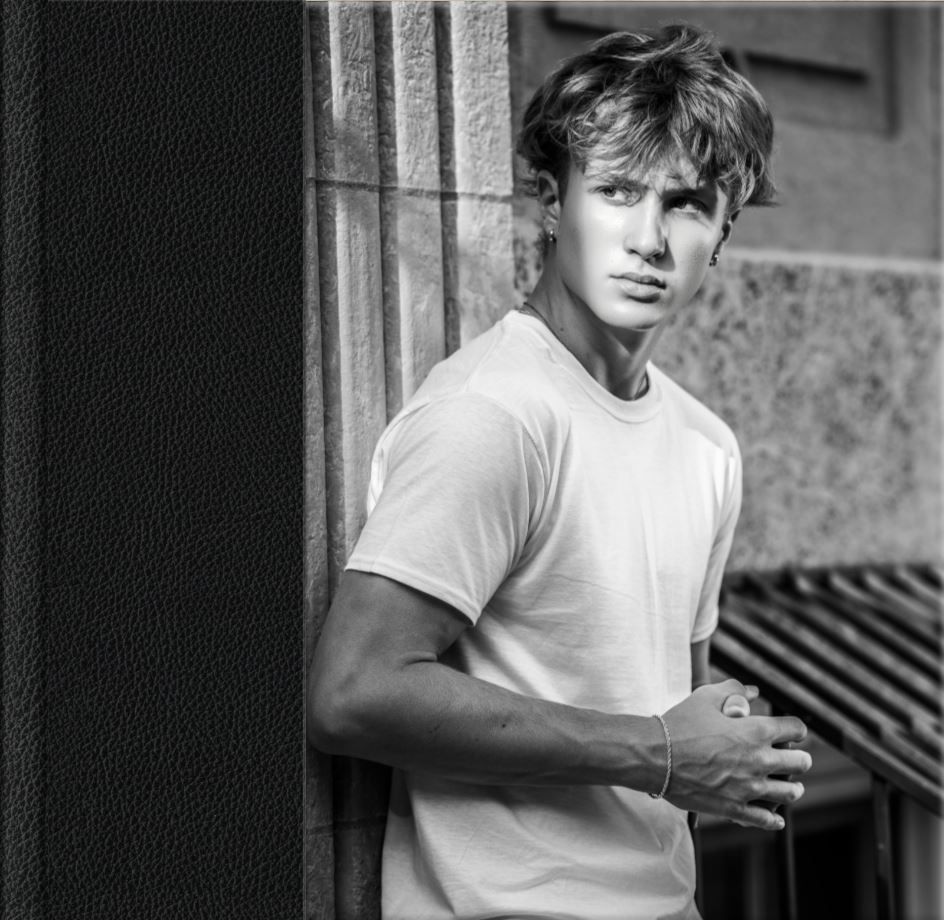 Young man in white t-shirt leaning against wall in black and white urban photo.