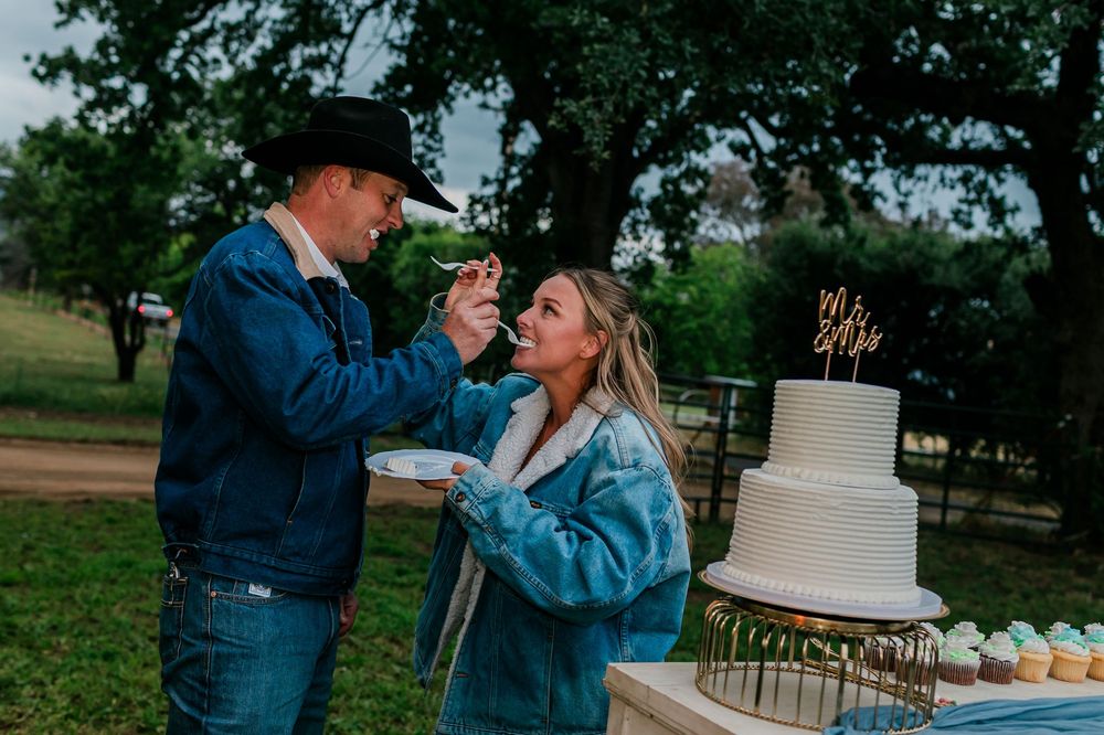 Couple sharing wedding cake outdoors at rustic country wedding celebration with white tiered cake.