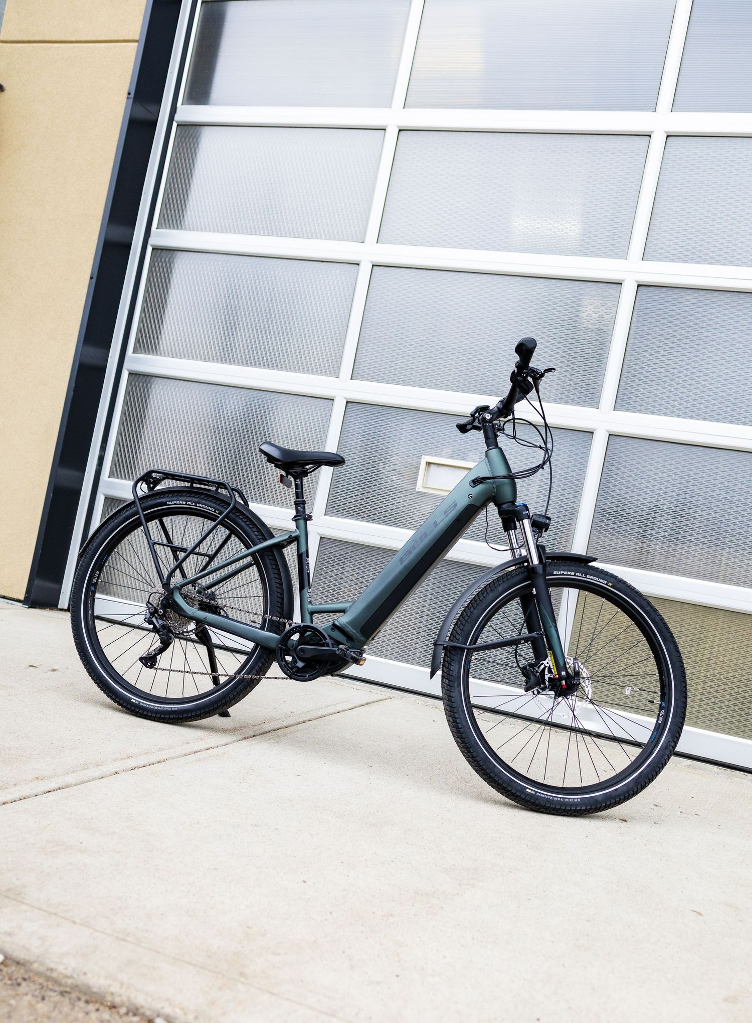 Dark green electric bike parked on a sidewalk in front of a modern building with large glass windows.