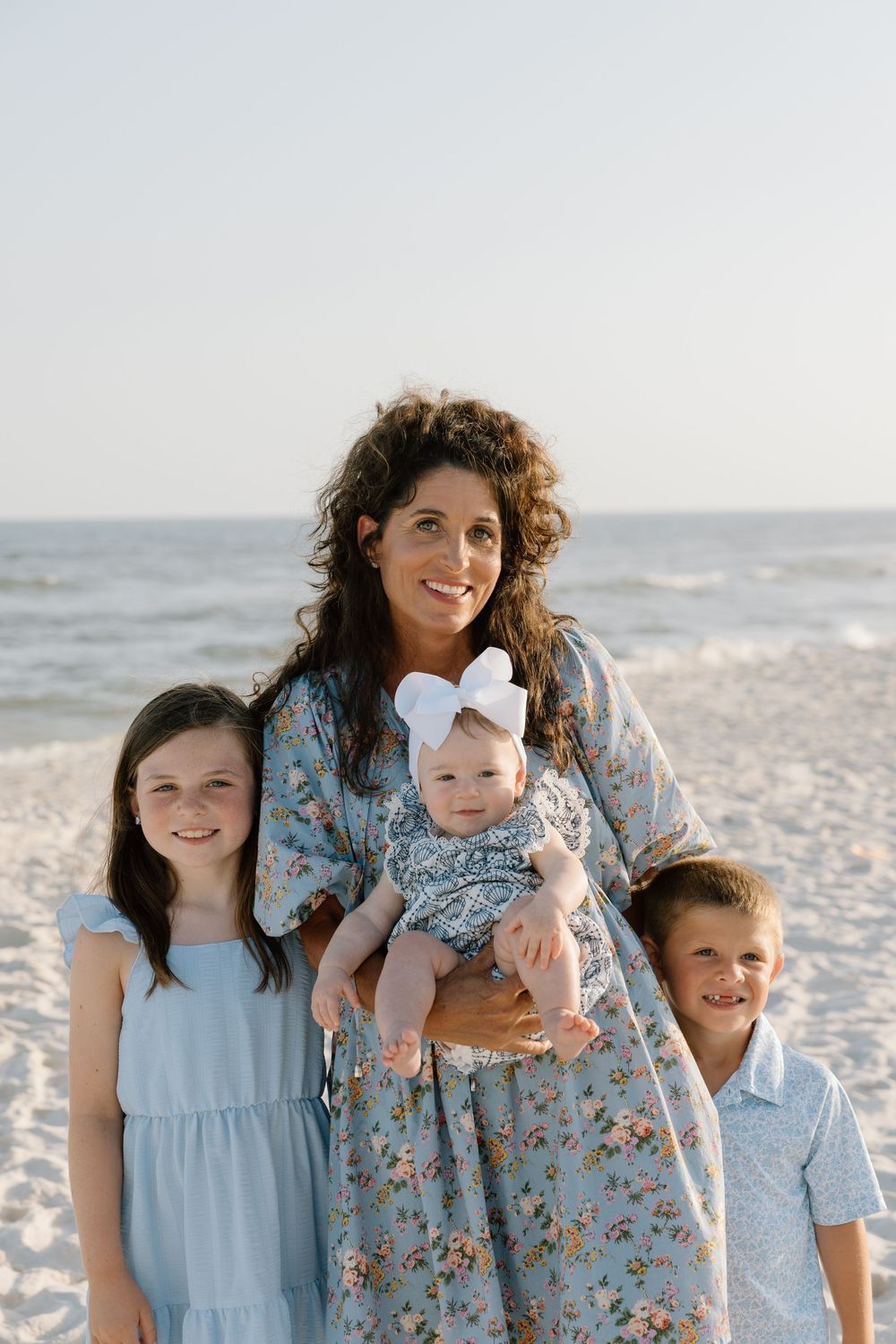 Family portrait of a couple and family holding their baby and kids on the beach in Orange Beach, Alabama.