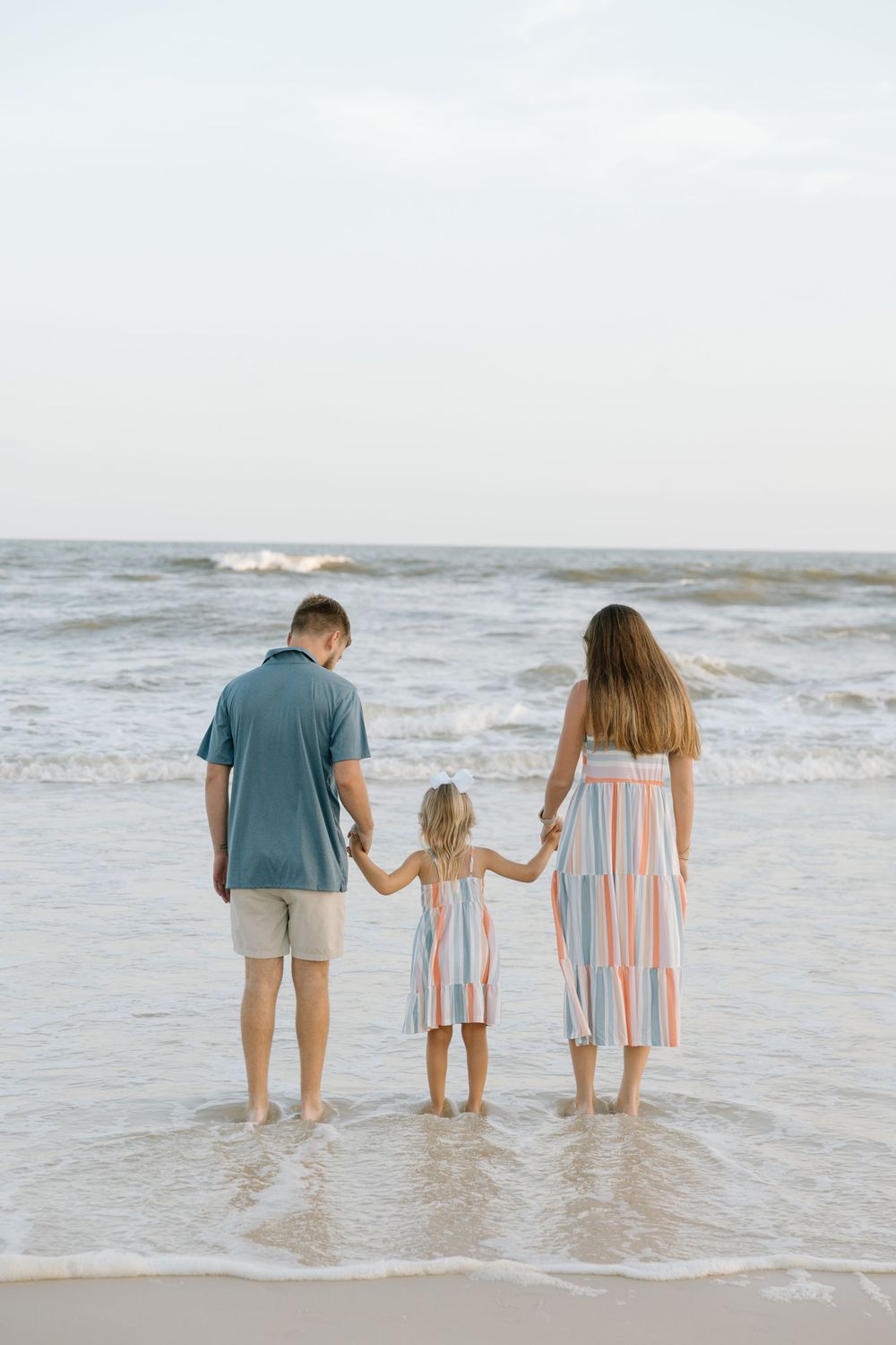 Mom dad and daughter walking into the water at the beach holding hands in Gulf Shores and Orange beach Alabama.