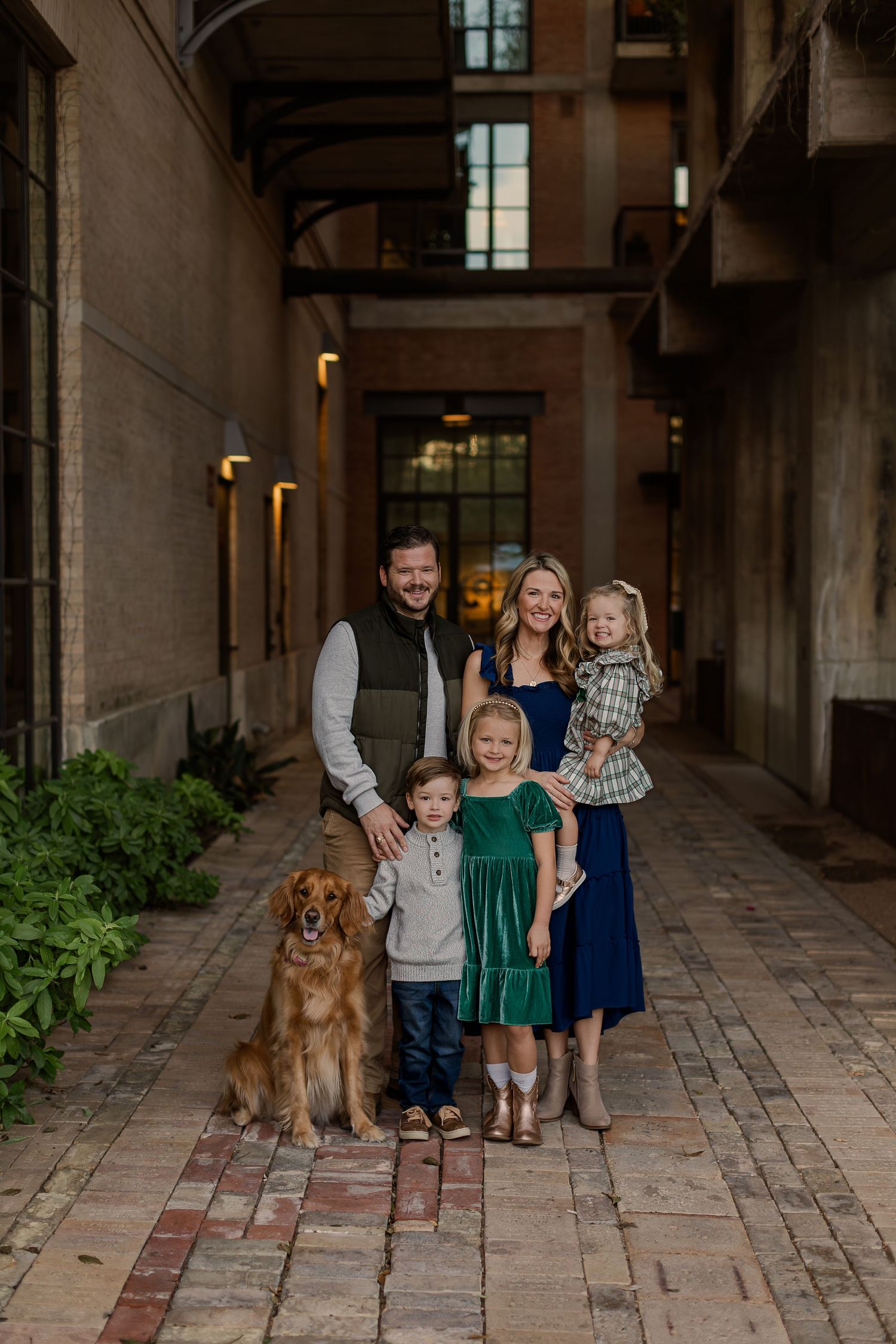 Family of four with a golden retriever posing in a charming brick alleyway, dressed in coordinated fall outfits.