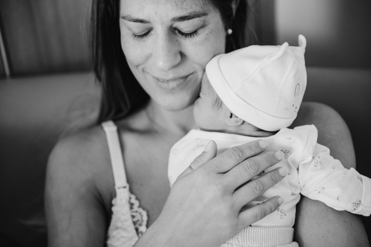 A mother tenderly holds her newborn baby dressed in white, sharing a gentle moment of bonding.
