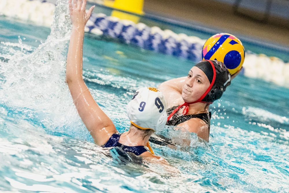 Female water polo player #9 reaches for the ball during an intense competitive match in an indoor pool.