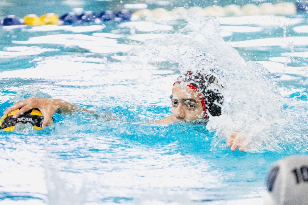 Water polo players compete intensely in an indoor pool with splashing water during a match.