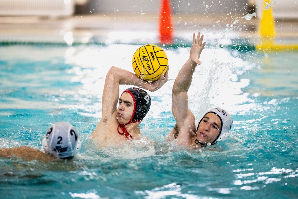 Male water polo players #2 compete for possession of a yellow ball during an indoor pool match.