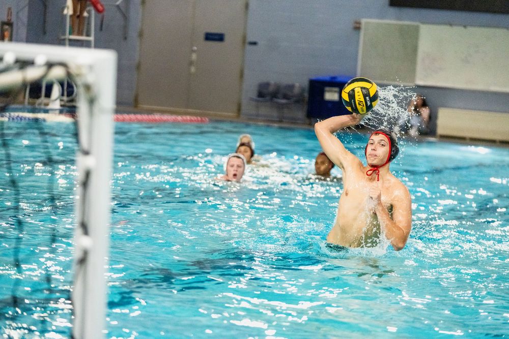 Water polo players compete in an indoor pool as one athlete winds up to throw the ball toward the goal.