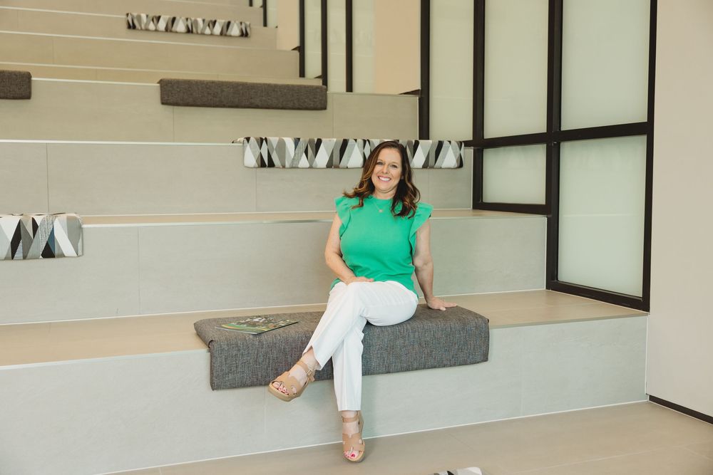 Woman in green top and white pants sitting on modern concrete bench in contemporary interior space.