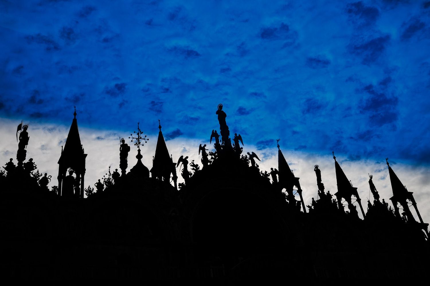 Dramatic silhouette of Gothic cathedral spires and statues against a deep blue twilight sky.