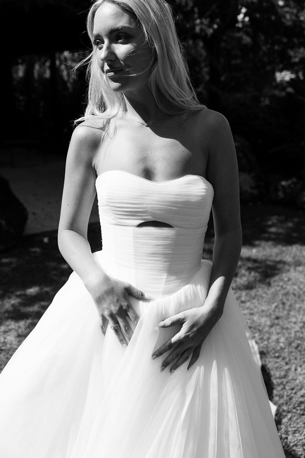 Black and white photo of a blonde bride in a strapless ball gown wedding dress posing outdoors.