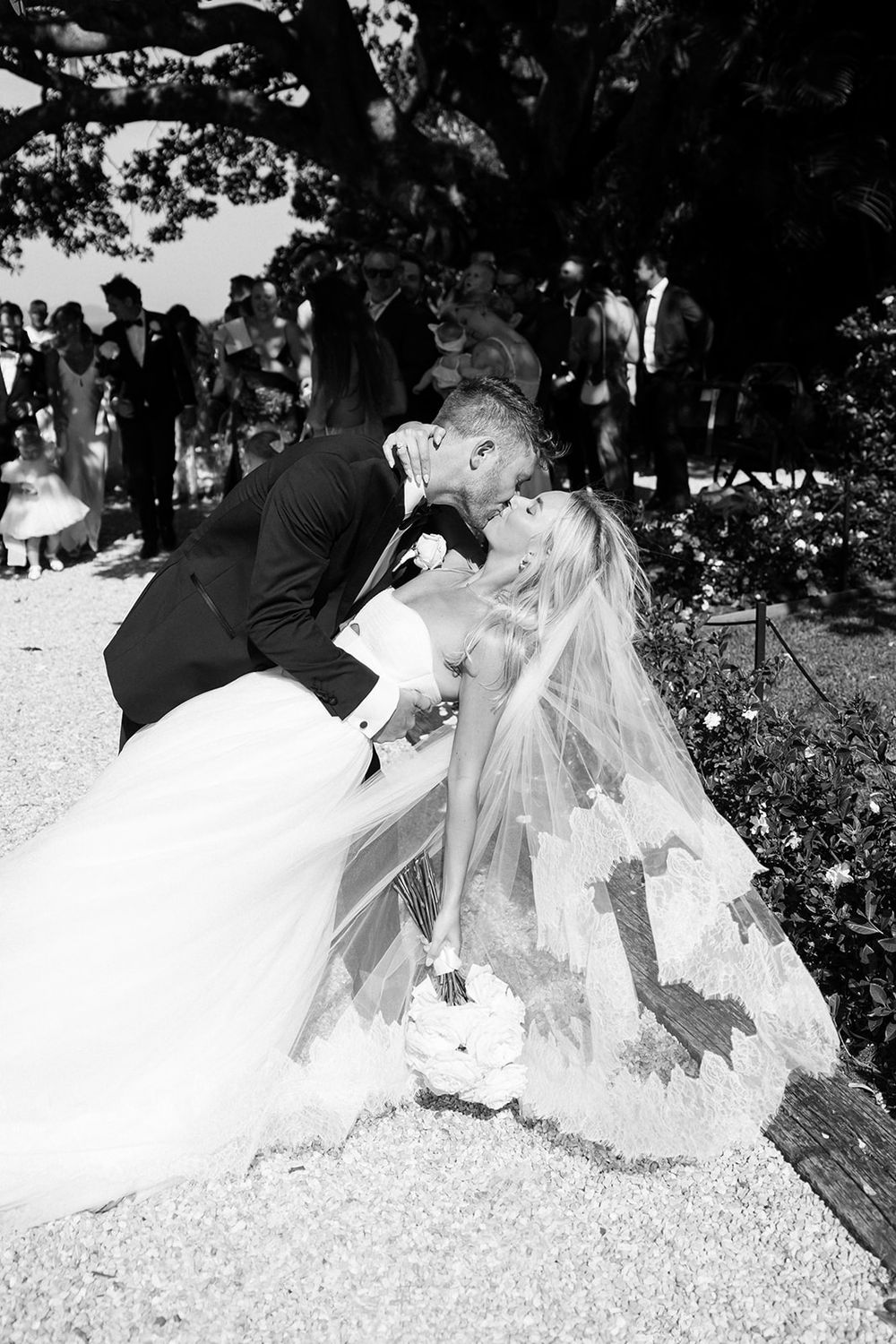Black and white photo of bride and groom sharing a romantic dip kiss at outdoor wedding ceremony.