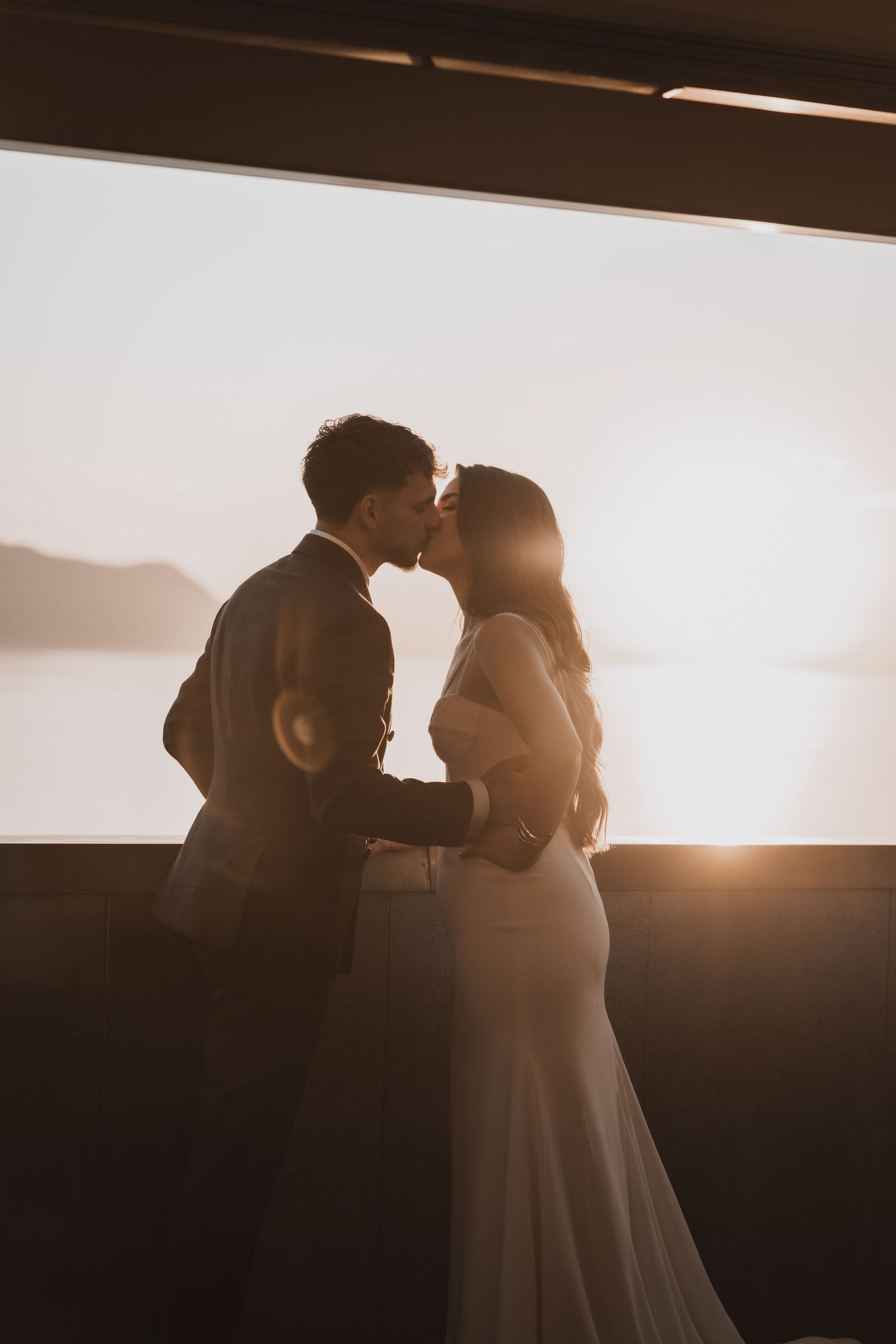 Couple de mariés s’embrassant au coucher du soleil sur une terrasse avec vue sur le lac