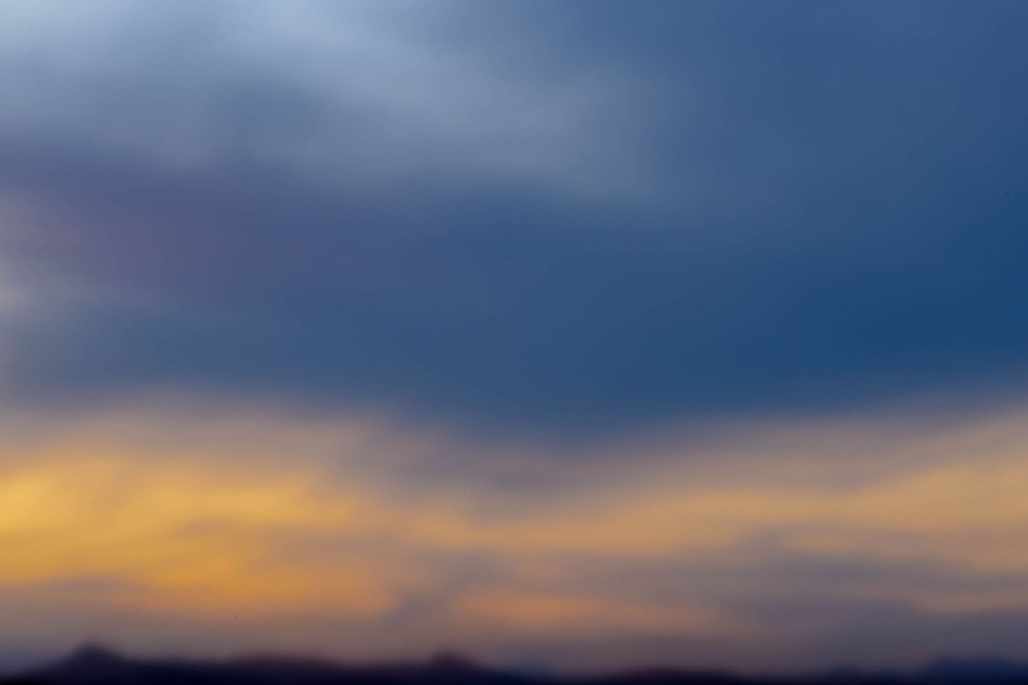 A dramatic sunset sky with deep blue clouds and golden orange hues over a silhouetted mountain horizon.