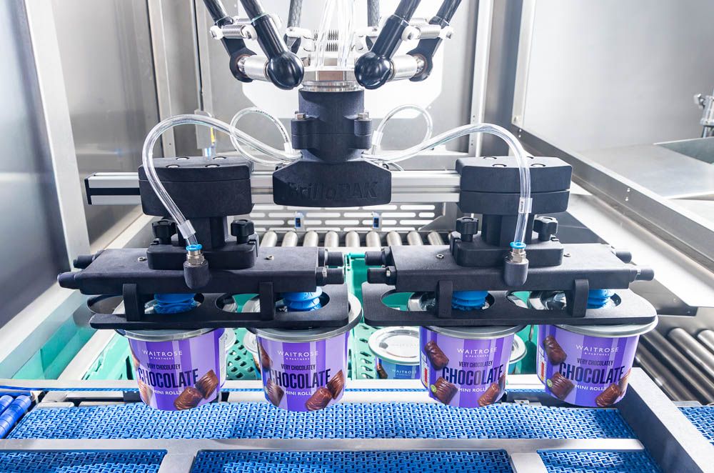 Automated packaging machinery filling purple labeled cups on a blue conveyor belt in a food production facility.