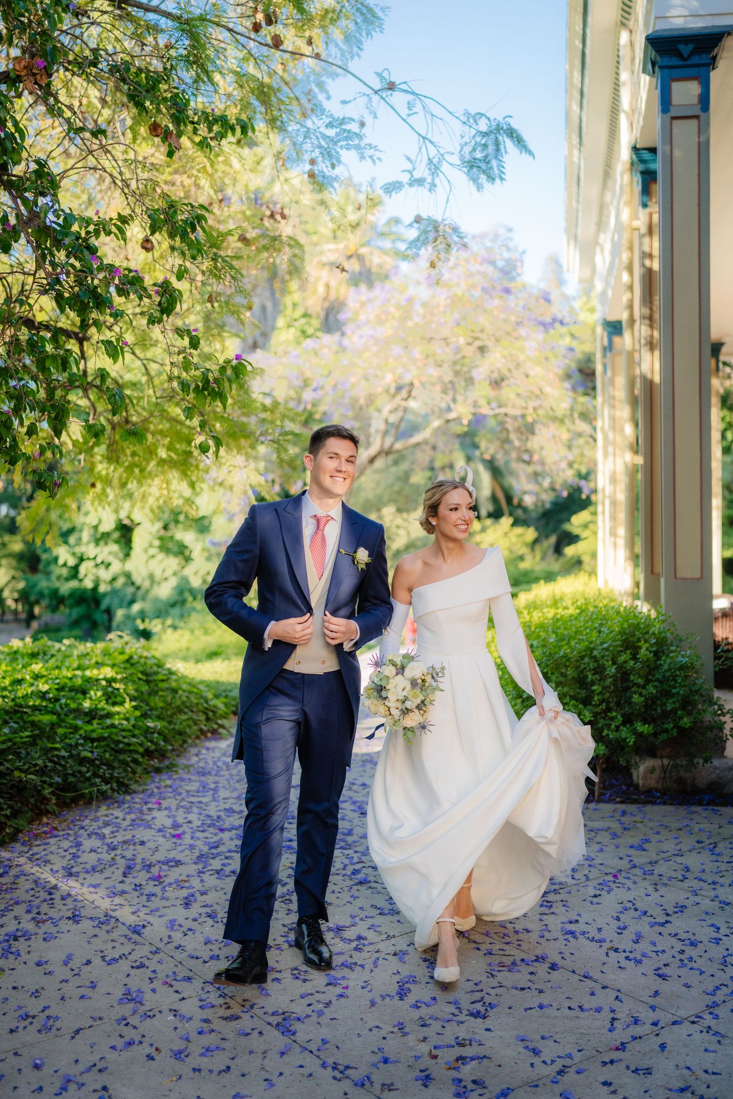 Bride and groom walking together on a petal-covered path surrounded by lush gardens on their wedding day.