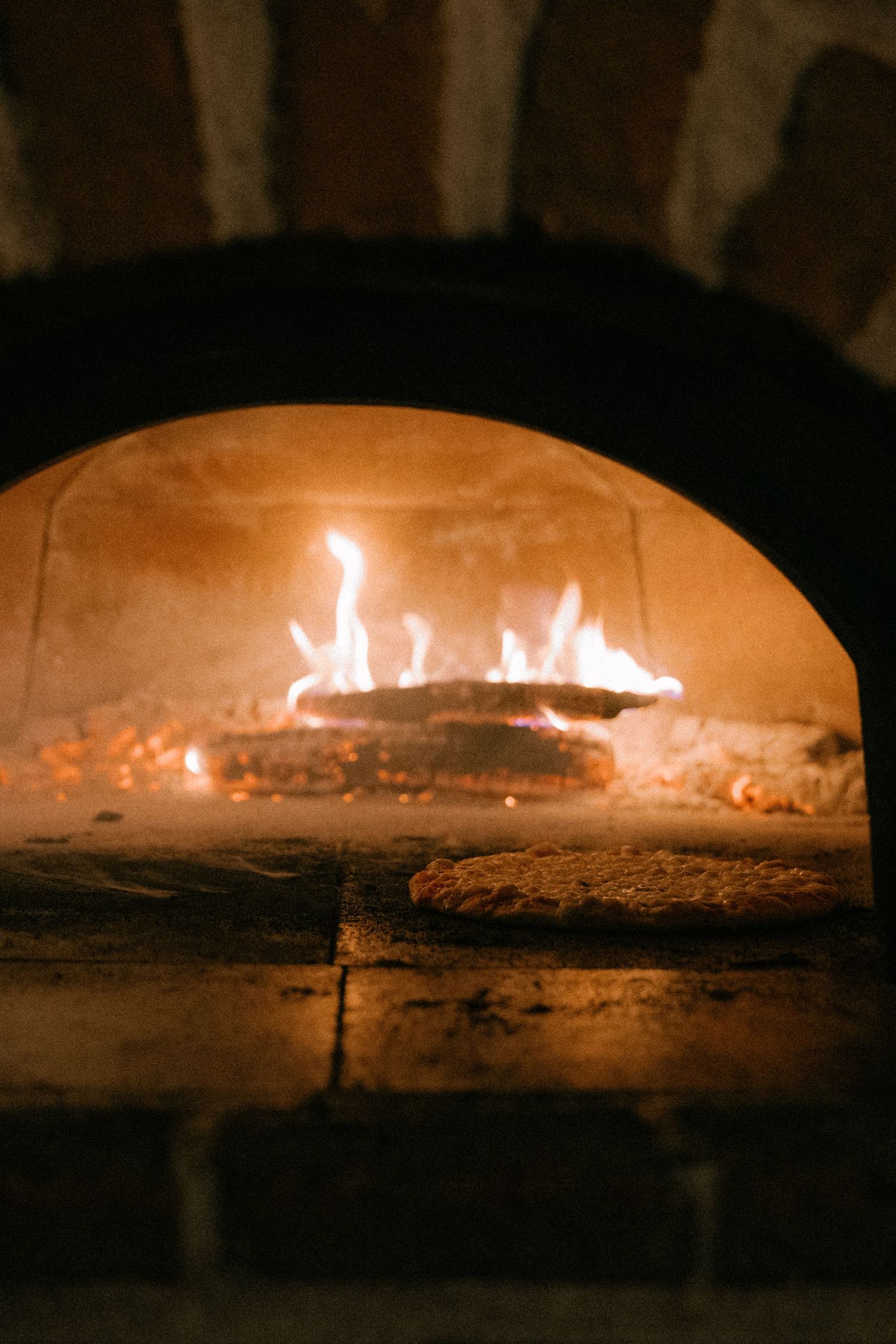 Pizza baking in a traditional wood-fired brick oven with glowing flames at a wedding reception.