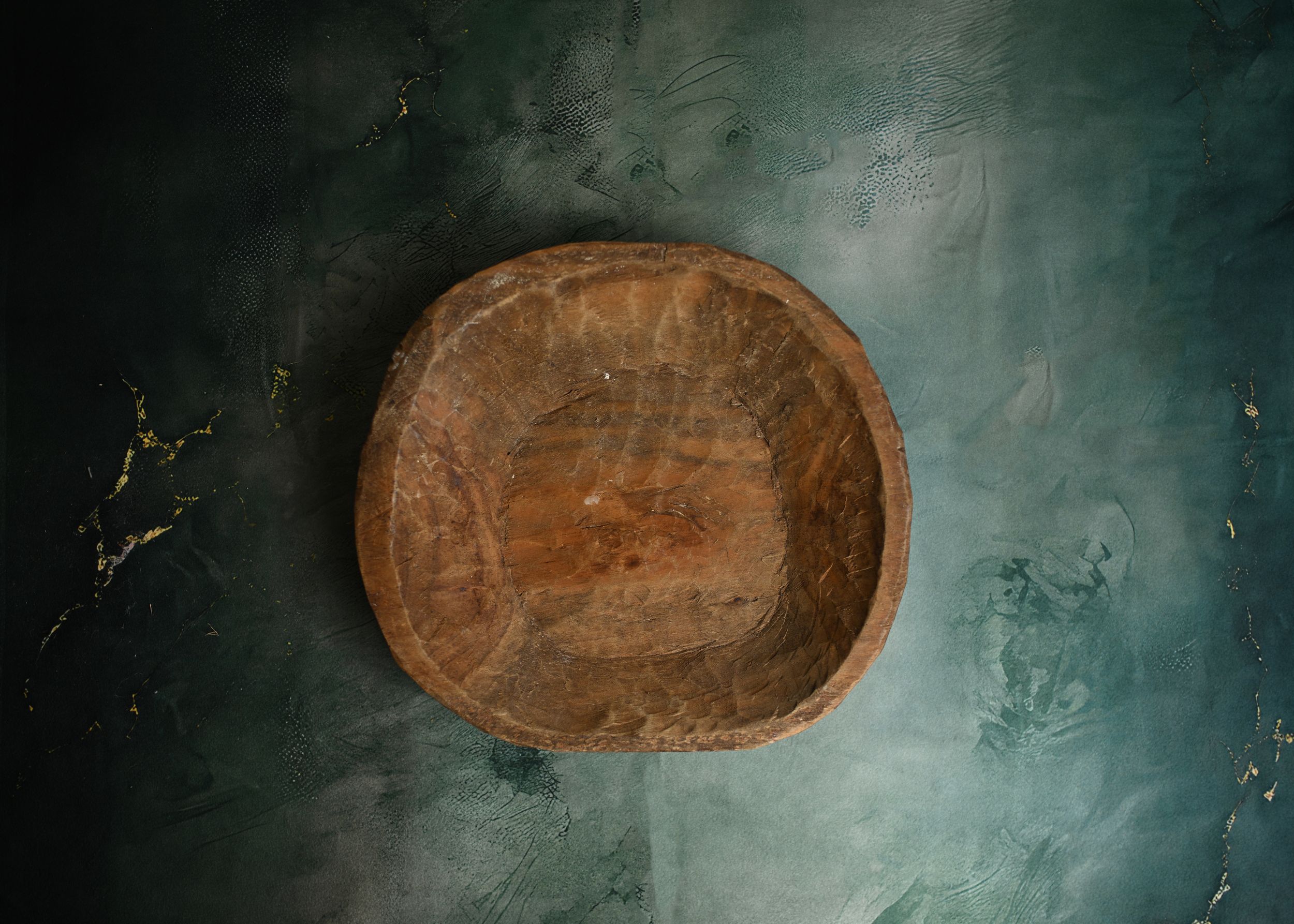Rustic handcrafted wooden bowl with natural grain texture, photographed on dark teal background.
