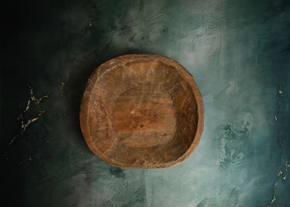 Rustic handcrafted wooden bowl with natural grain texture, photographed on dark teal background.