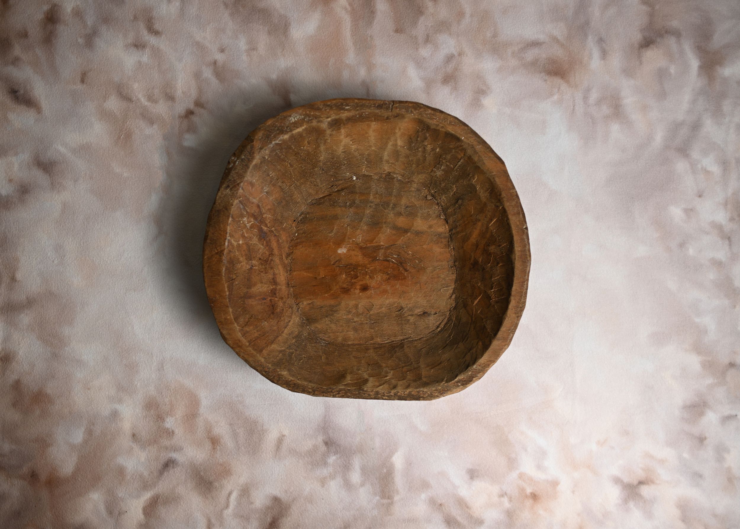 Rustic handcrafted wooden bowl with natural grain texture, aged patina finish, displayed on marble surface.