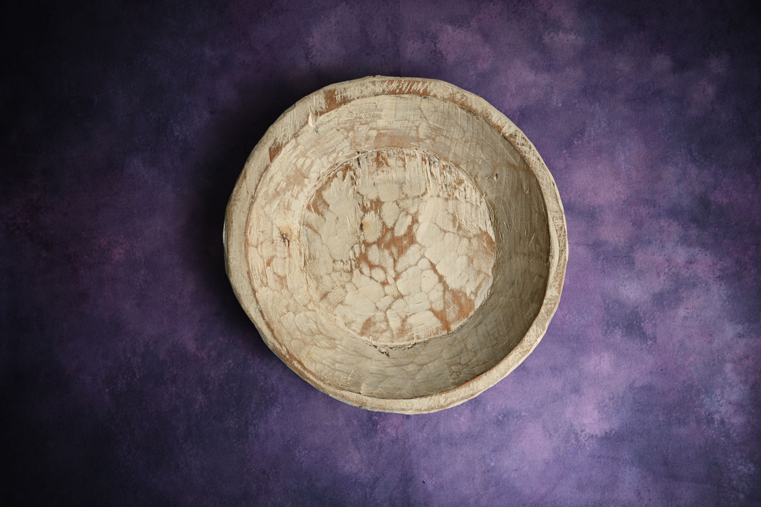 Rustic handmade ceramic bowl with marbled beige and brown glaze on purple textured background.