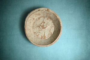 Antique rustic ceramic bowl with crackled patina finish, photographed from above on teal background.