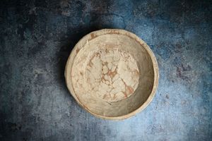 Rustic handmade ceramic bowl with natural earthy tones on a dark textured background.
