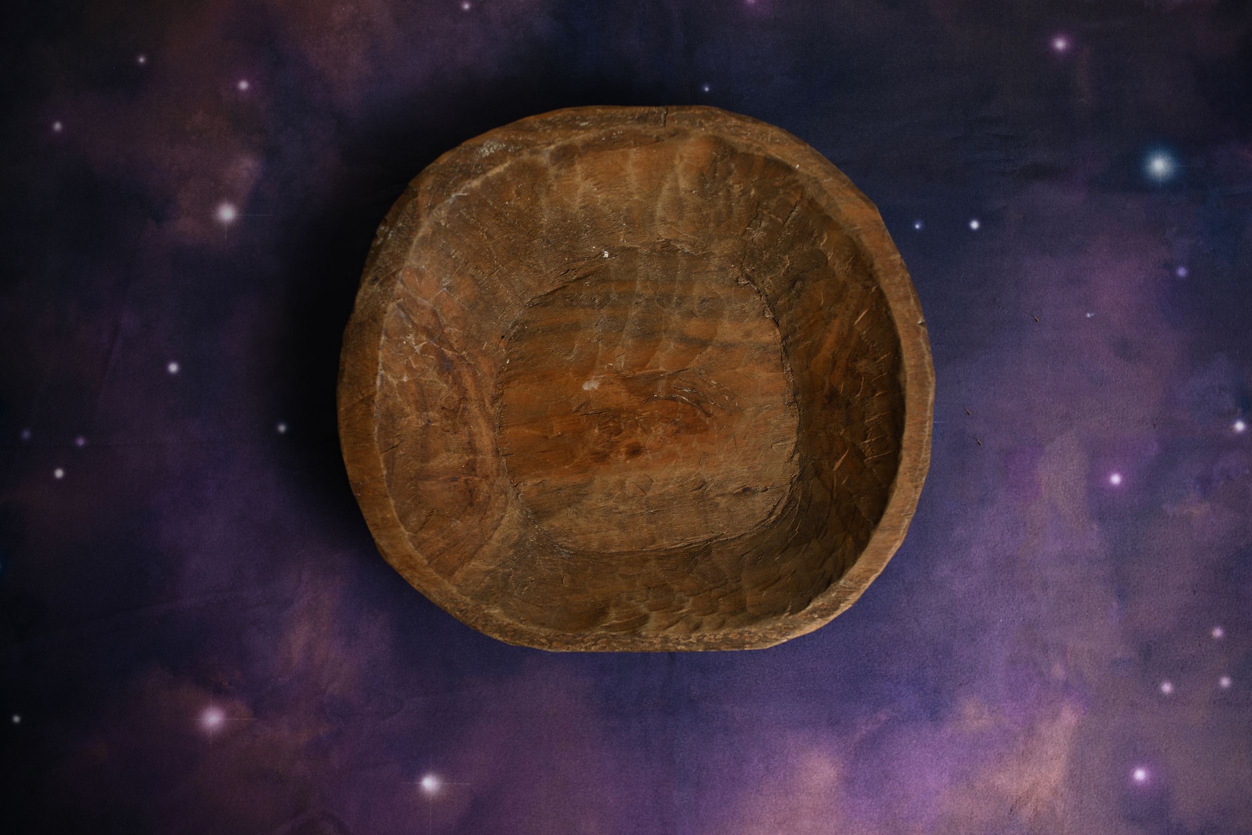 Rustic antique wooden bowl on a purple cosmic galaxy background with stars.