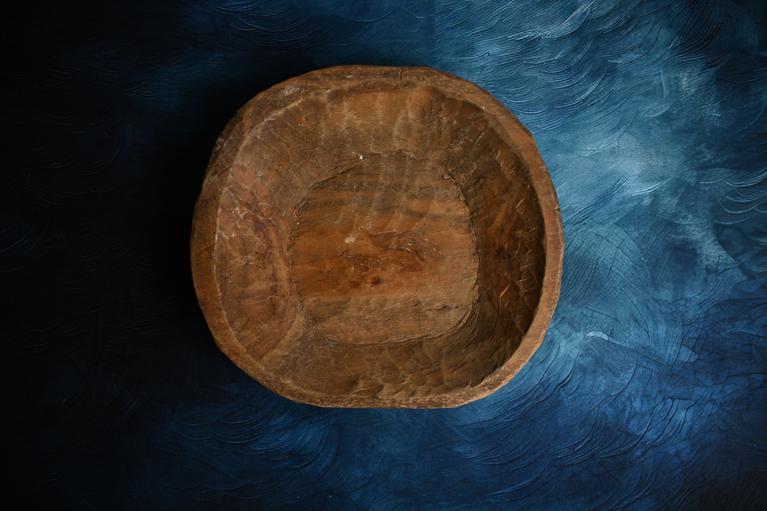 Rustic handcrafted wooden bowl with natural grain texture on dark blue background.