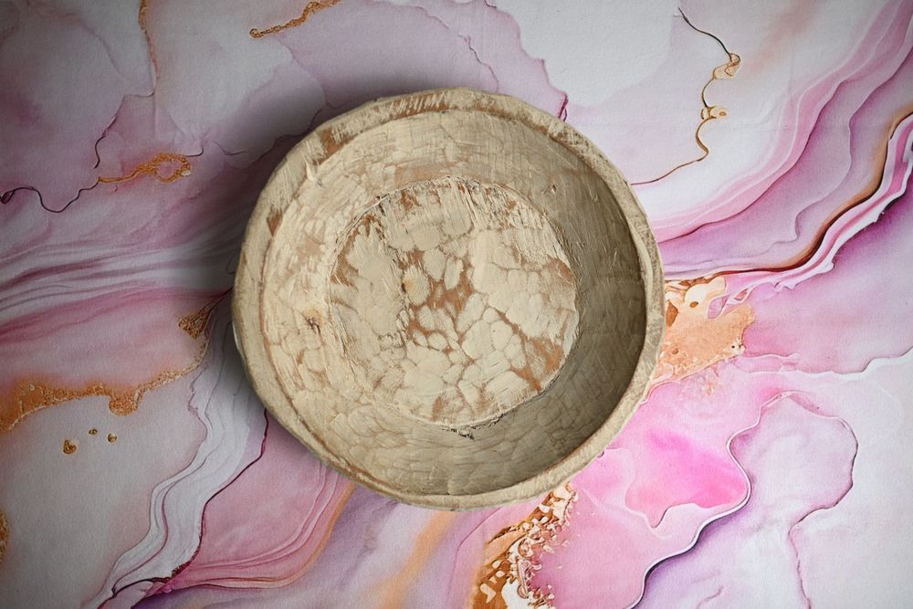 A rustic marble bowl with beige and brown tones resting on a pink and gold fluid art marble surface.
