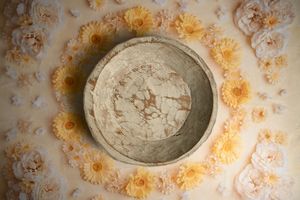 Stone bowl surrounded by a circle of soft yellow and cream flowers on a light floral background.