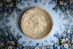 Rustic handmade wooden bowl on a blue floral fabric background with delicate white and blue flowers.