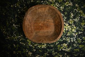 Rustic wooden bowl on dark floral background with white blooms and green leaves.