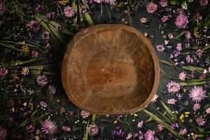 Rustic wooden bowl surrounded by colorful wildflowers and green stems on a dark background.