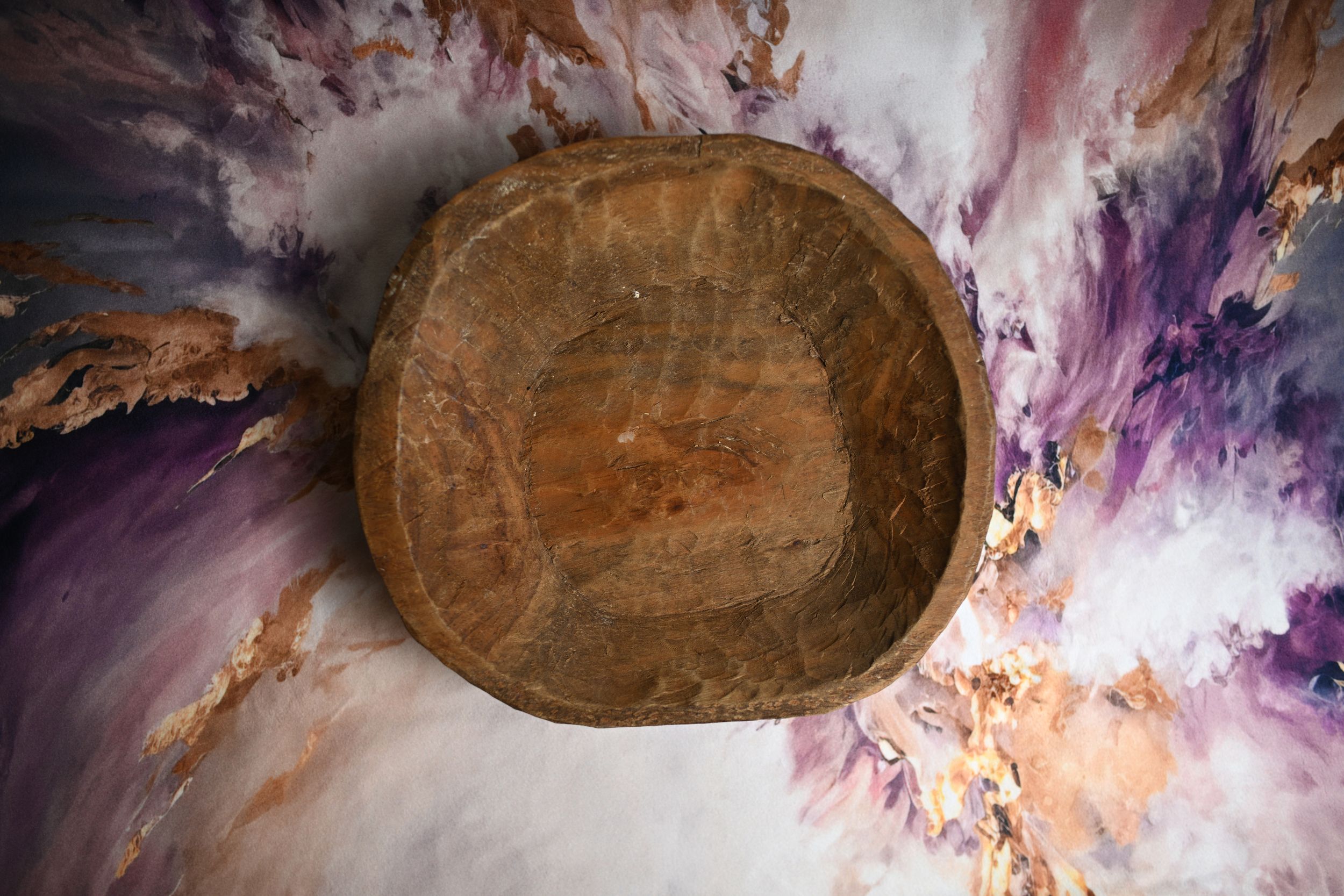 Rustic wooden dough bowl displayed on a vibrant purple and white abstract painted background.