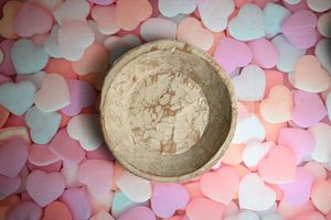 A rustic ceramic bowl surrounded by colorful pastel candy hearts on a pink background.