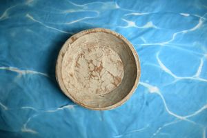 Rustic handmade ceramic bowl with marbled texture resting on a blue water-patterned fabric background.