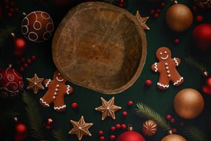 Festive Christmas flatlay with gingerbread cookies, ornaments, pine branches, red berries, and a rustic wooden bowl on green background.