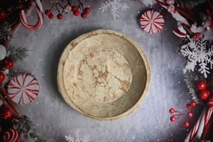 Rustic wooden bowl surrounded by festive Christmas decorations including candy canes, red berries, and snowflakes.
