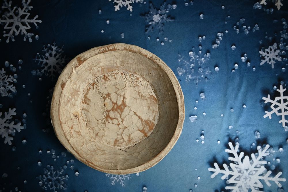 Rustic wooden bowl with cracked texture on blue fabric surrounded by white decorative snowflakes.