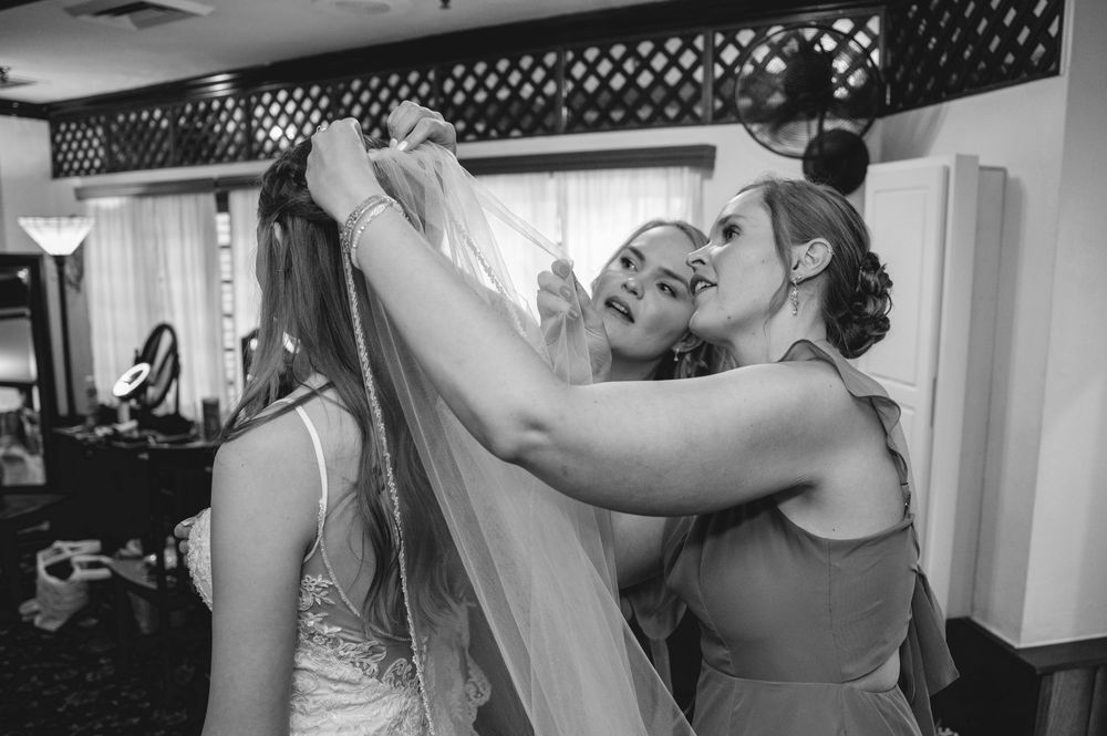 Bridesmaids helping bride with veil in black and white wedding preparation photo.