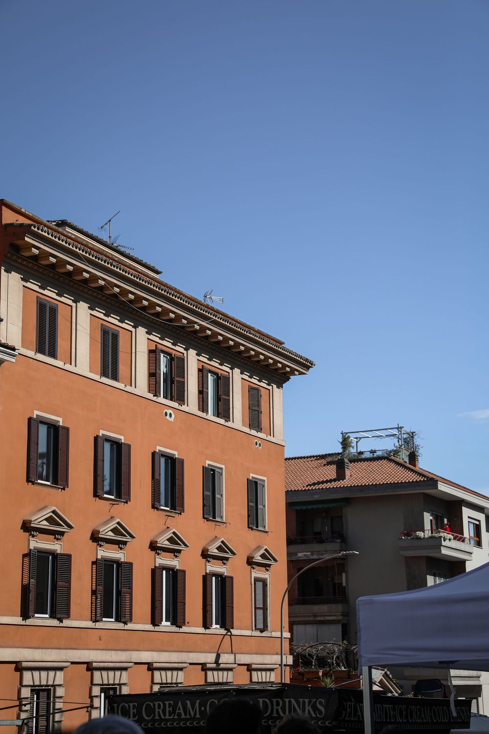 Orange terracotta Italian building with green shuttered windows against a clear blue sky in Rome.