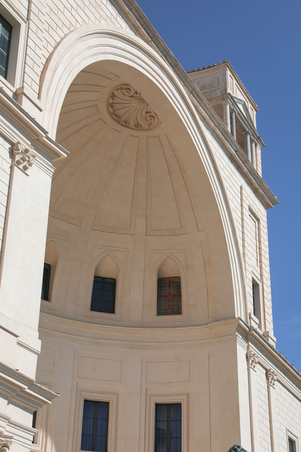 Neoclassical building facade featuring an ornate arched entrance with shell motif detail against a clear blue sky.
