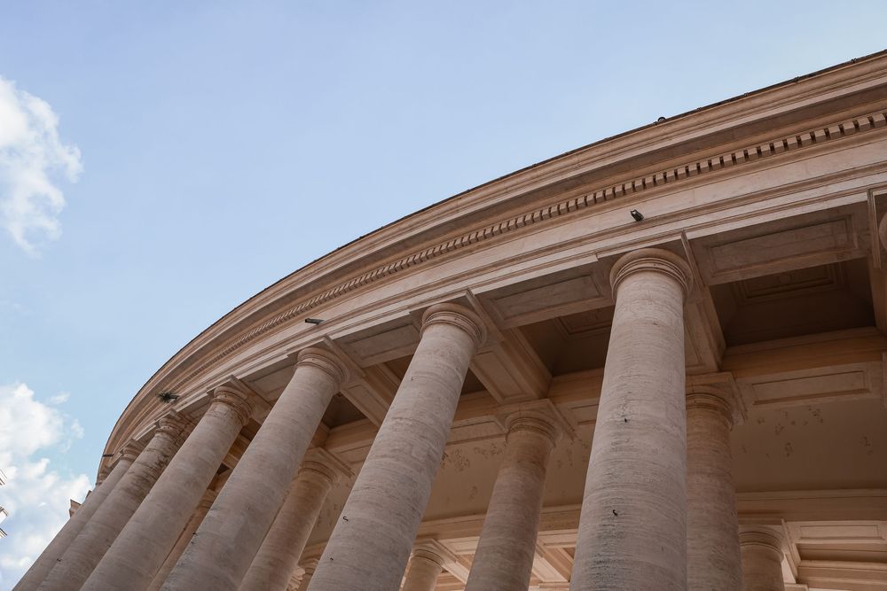 Neoclassical building with tall stone columns and curved facade against a blue sky, Jefferson Memorial, Washington DC.