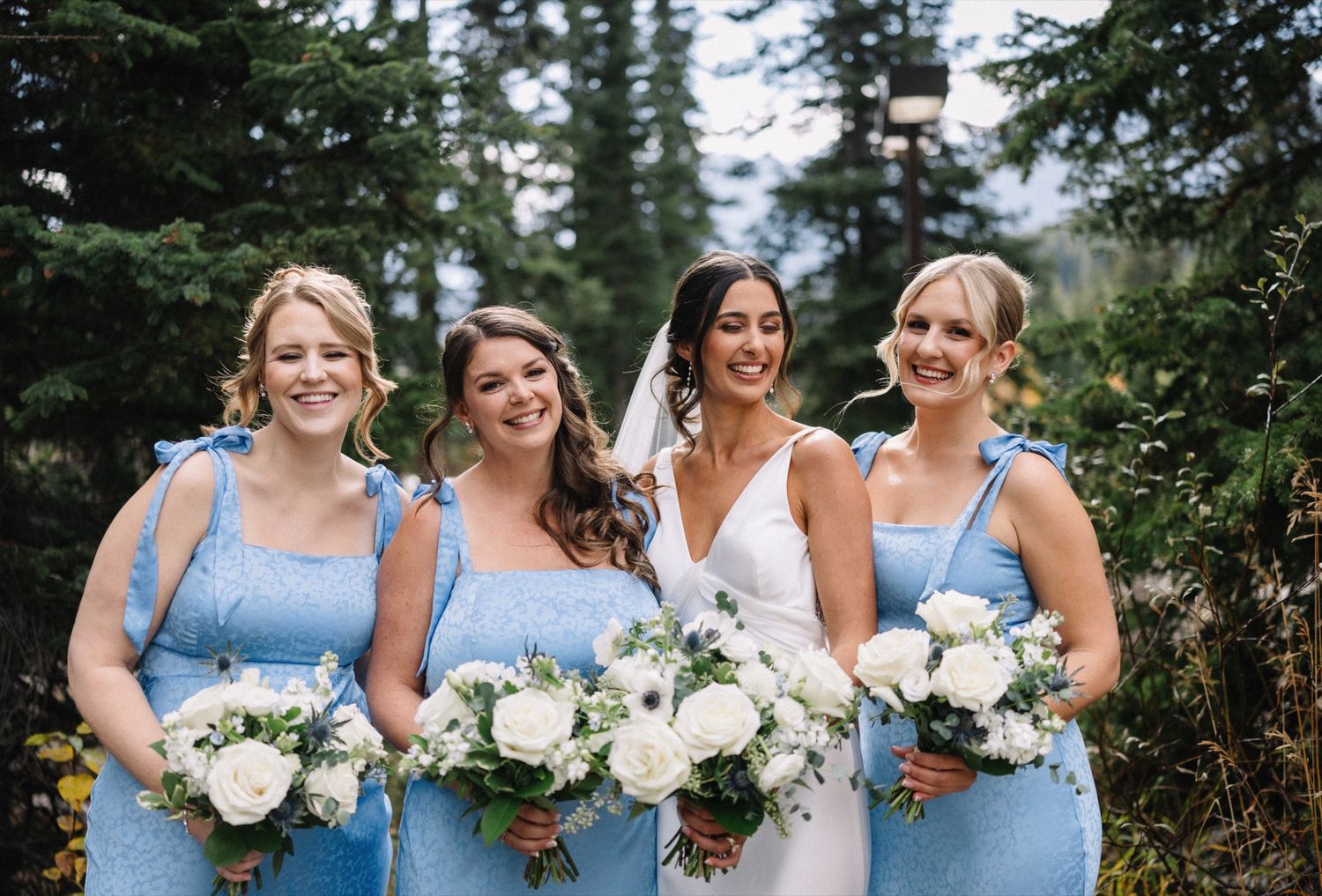 Bride and bridesmaids in dusty blue among fall trees in Lake Louise