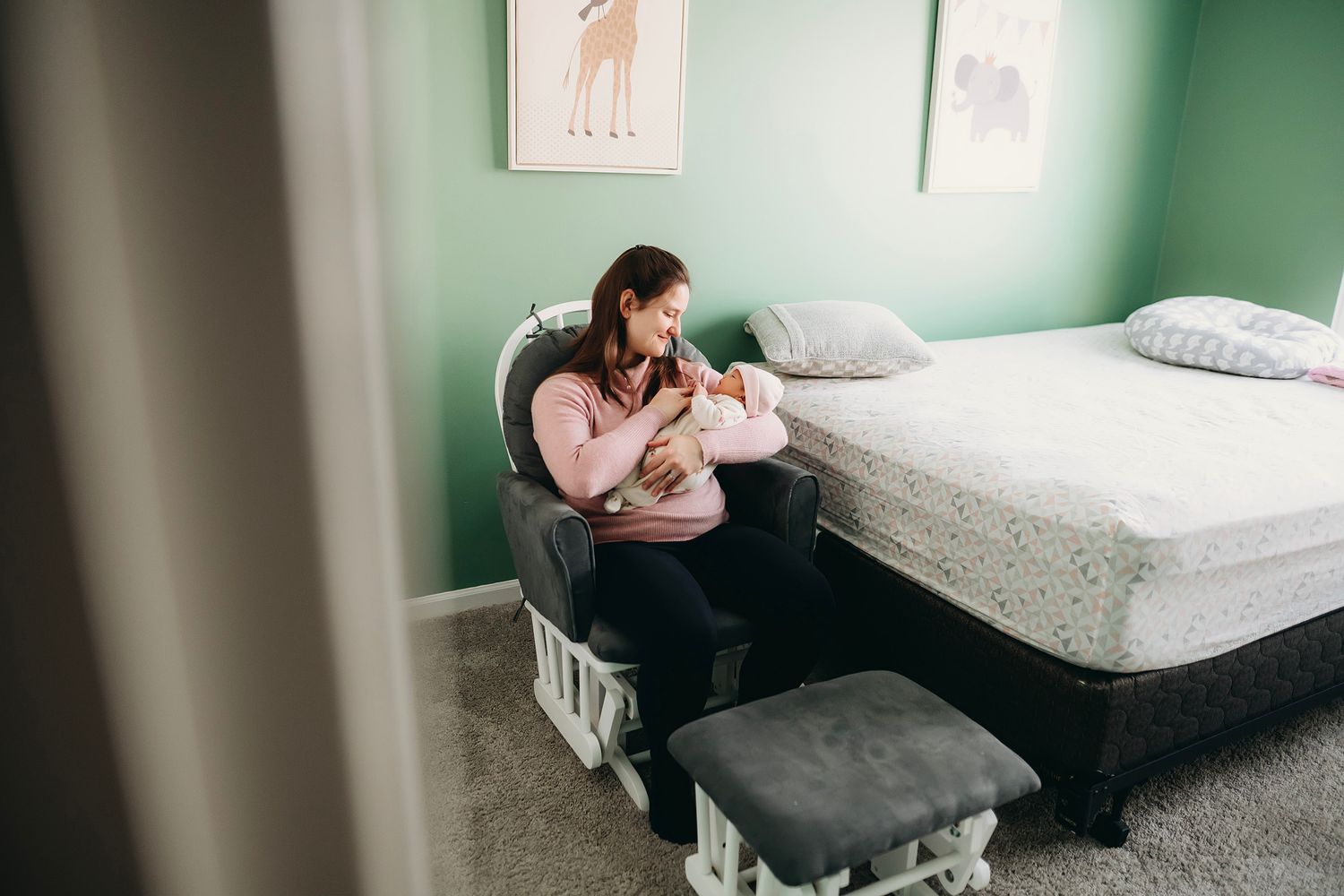 Mother sitting in a rocking chair breastfeeding her newborn baby in a cozy green nursery bedroom.