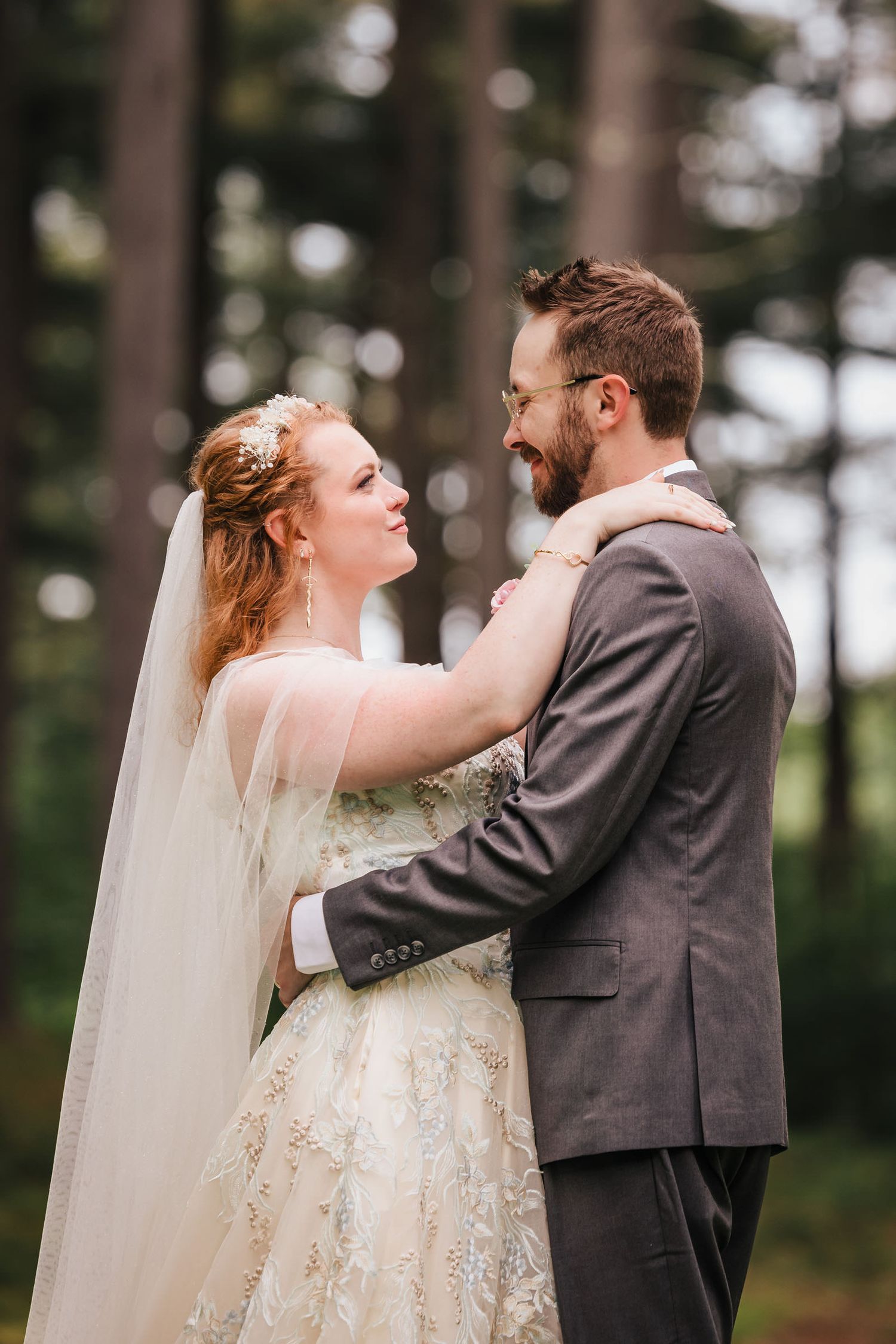 Bride with her arms around the groom's neck, both laughing closely together in the trees.