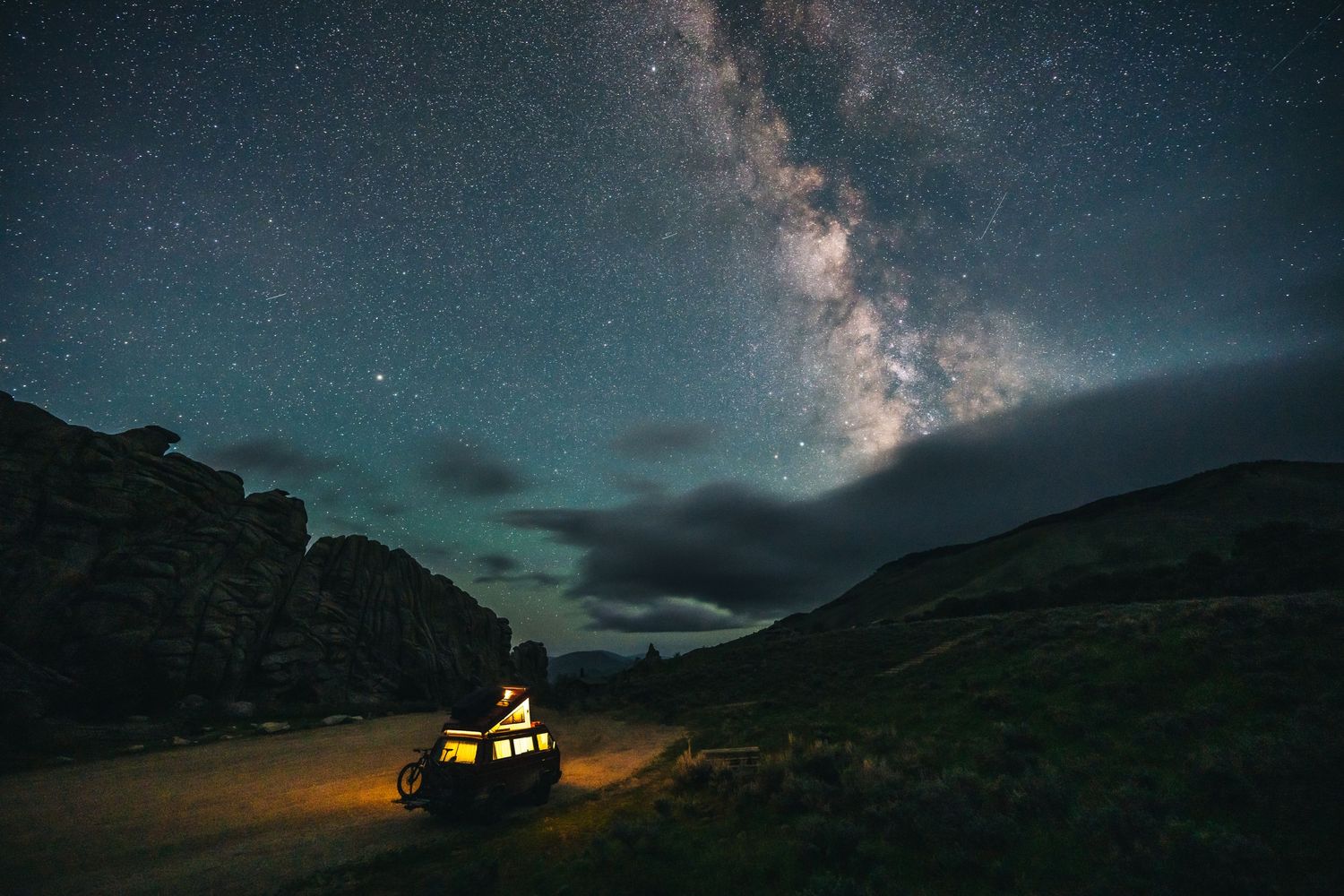 Vehicle under starry night sky with Milky Way galaxy visible between mountain ridges.